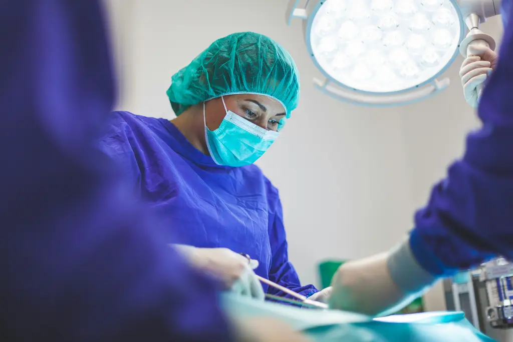 A woman wearing a green mask and a sugery scrubs while performing a surgery.